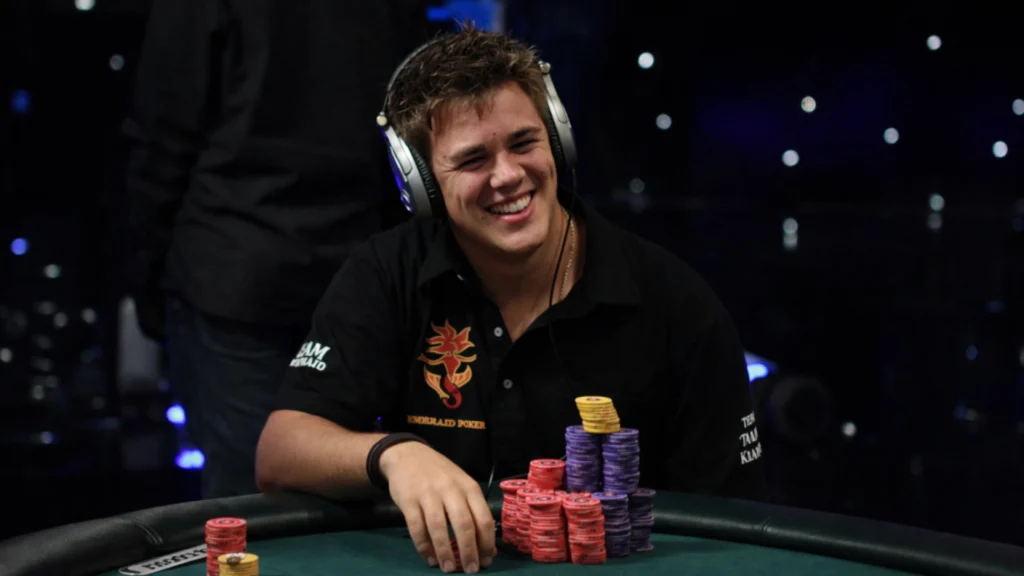 Pokerproffen Jonas Klausen smiler ved pokerbordet med høretelefoner og store stakke chips