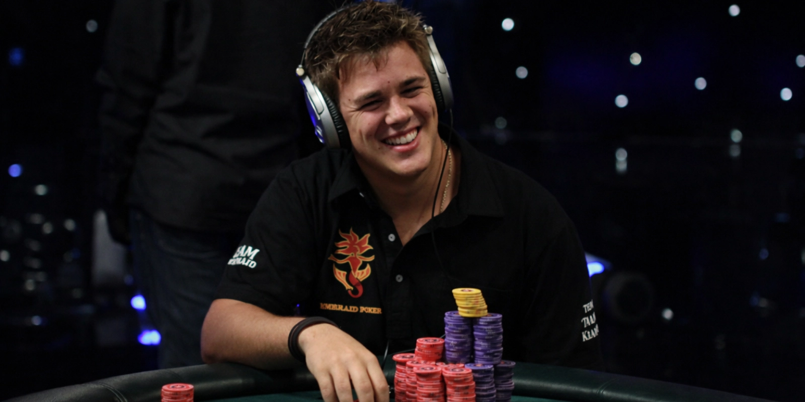 Pokerproffen Jonas Klausen smiler ved pokerbordet med høretelefoner og store stakke chips